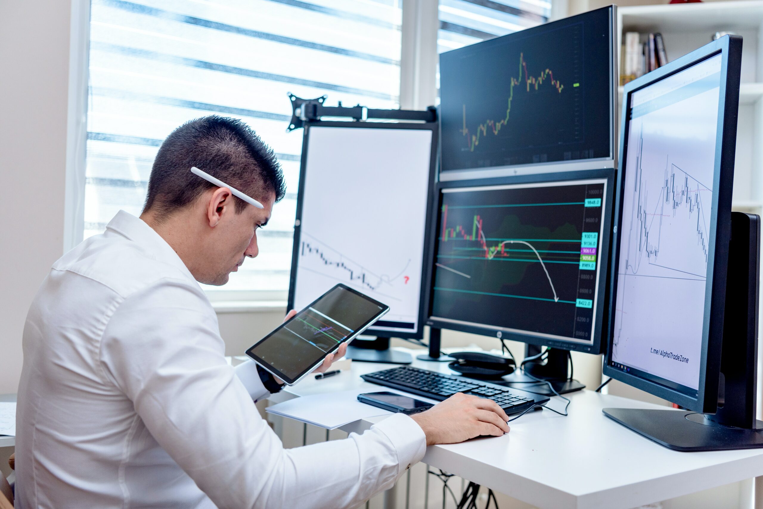 Mann mit weißem Hemd am Schreibtisch mit mehreren Monitoren auf denen jeweils Charts angezeigt werden
