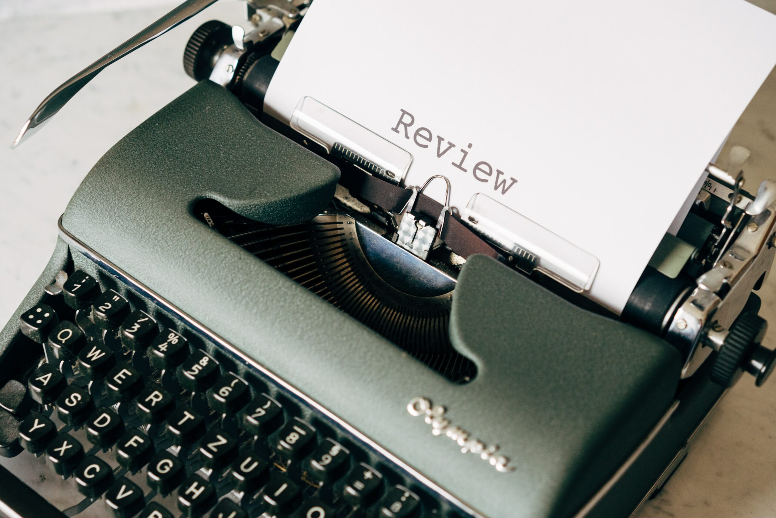 Grüne Schreibmaschine mit einem Blatt darin. Darauf steht der Begriff "Review"
