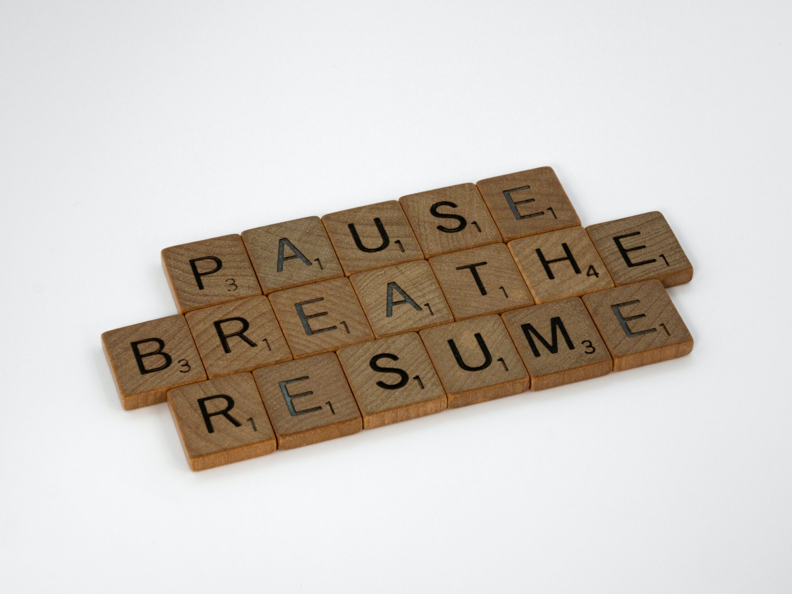 Weiße Fläche, auf der mehrere Holzsteinchen mit Buchstaben darauf liegen. Die Buchstaben ergeben die Worte "Pause", "Breathe" und "Resume".