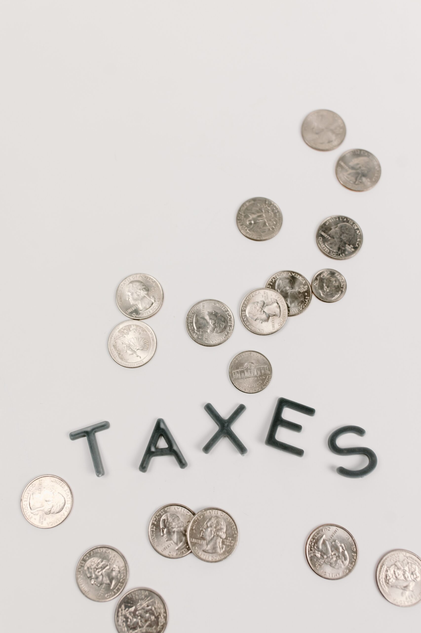 Wort Taxes auf einer weißen Fläche mit mehreren Münzen außenrum
