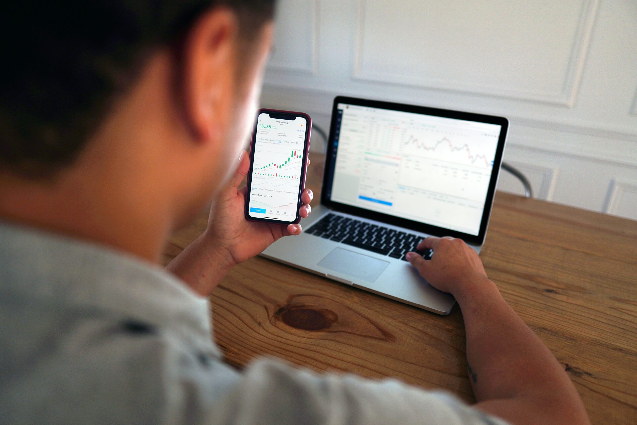 Mann mit Smartphone in der Hand betrachtet Charts im Trading Simulator im Laptop