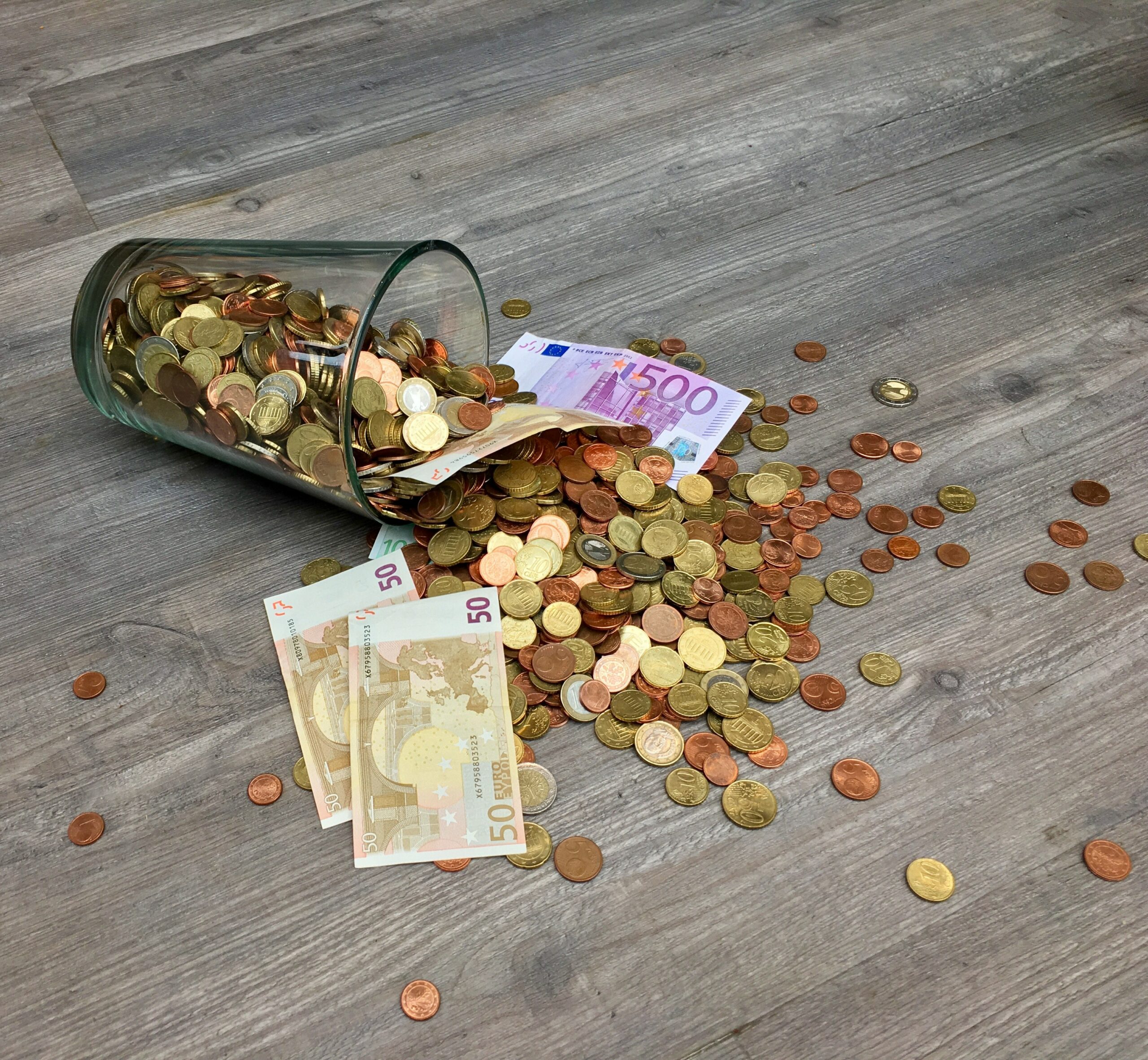 Auf der Seite liegendes mit Münzen gefülltes Glas mit drei 50 Euro Scheinen und einem 500 Euro Schein