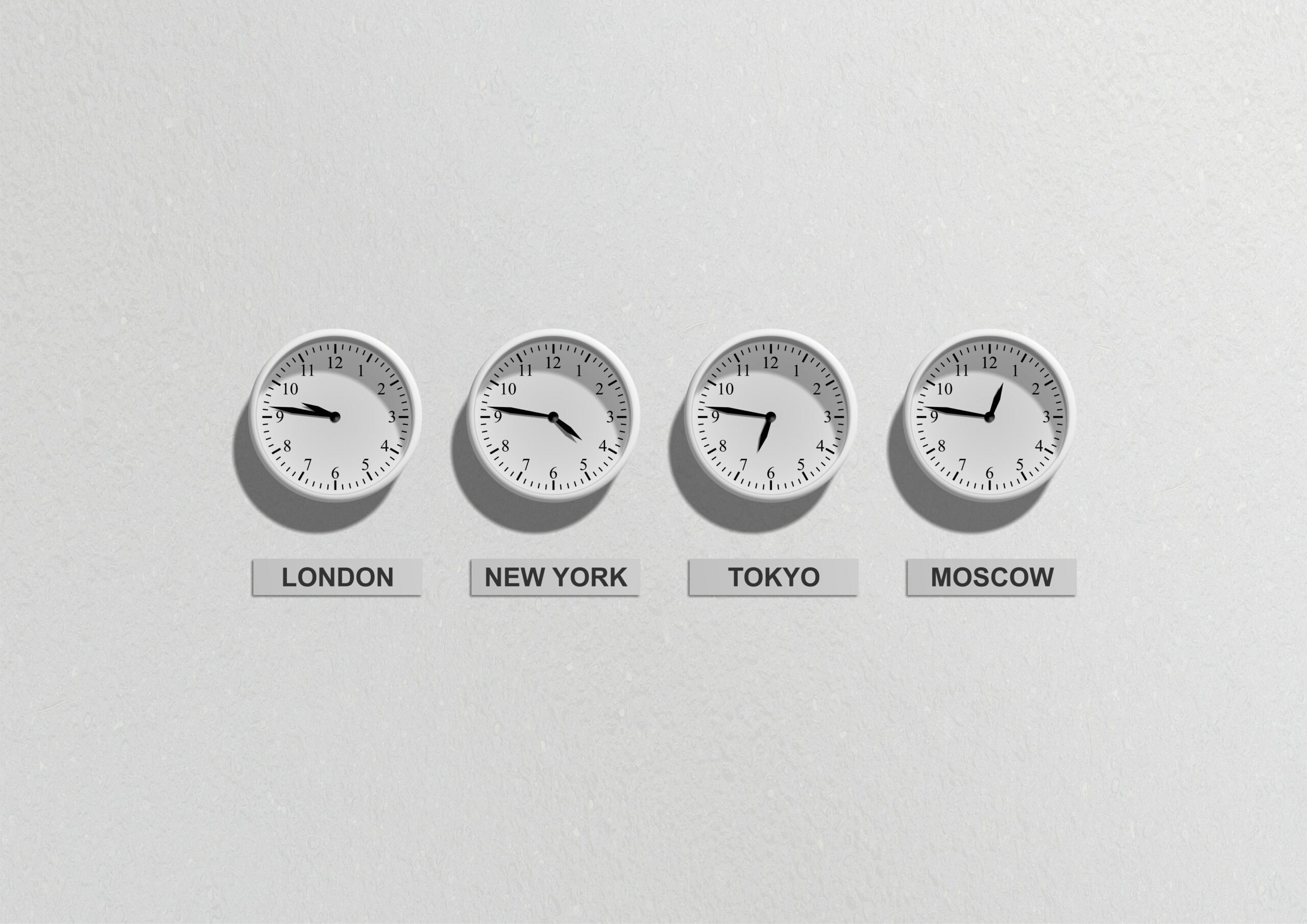 Weiße Wand, an der vier Uhren hängen. Sie zeigen unterschiedliche Uhrzeiten an und darunter hängt jeweils ein Schild mit der dazugehörigen Stadt.